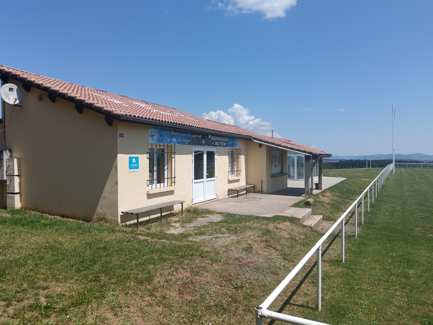Le bâtiment des vestiaires du stade communal, avec le terrain de football en herbe sur la droite