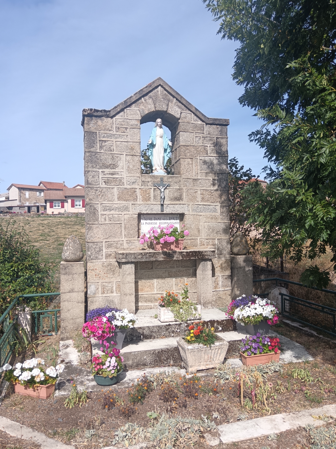 L'oratoire de Notre-Dame de la Route : statue de la Vierge dans une niche de granit, parterre de fleurs au pied du monument
